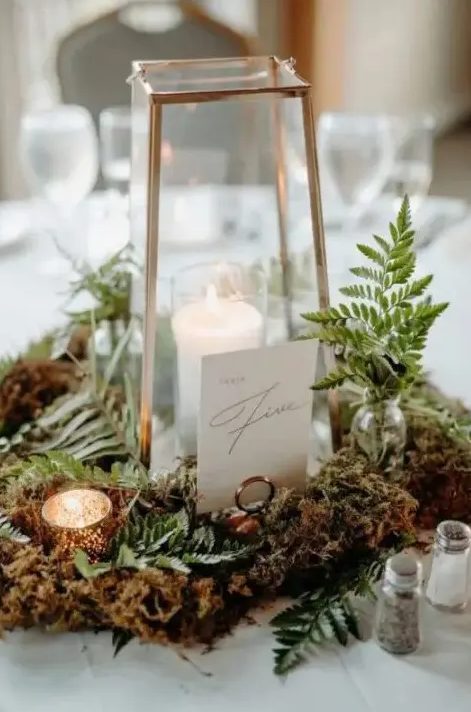 a woodland wedding centerpiece with moss, ferns, candleholders and a candle lantern plus a table number is very chic and beautiful