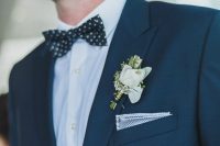 an elegant groom’s look with a black suit, a white shirt, a black polka dot bow tie and a polka dot handkerchief, a white boutonniere