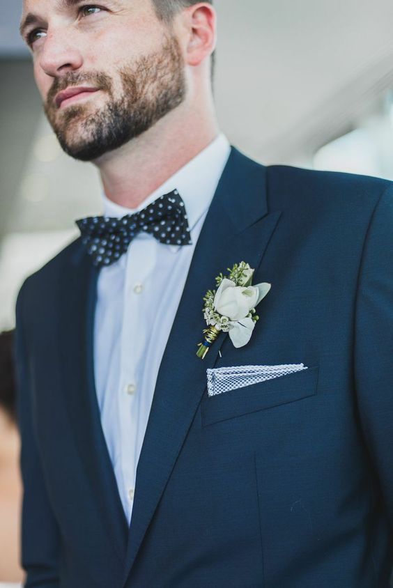 An elegant groom's look with a black suit, a white shirt, a black polka dot bow tie and a polka dot handkerchief, a white boutonniere