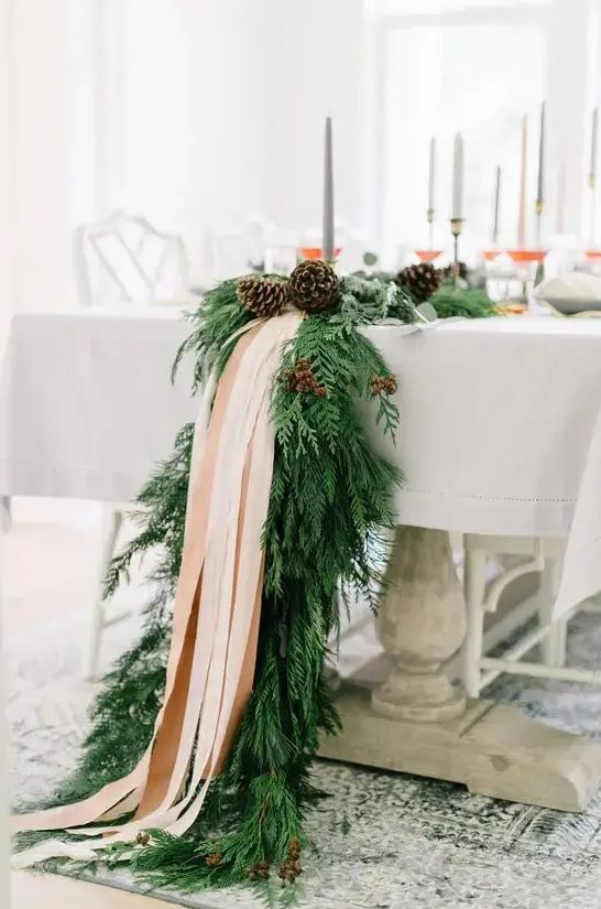 an exquisite winter table runner of evergreens, pinecones and blush ribbons will fit even the most refined winter wedding and will give ti a cozy feel