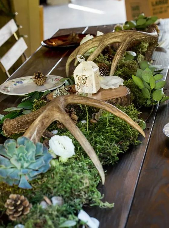 woodland wedding table decor with moss, succulents, pinecones, antlers, greenery and a tiny candle lantern on top