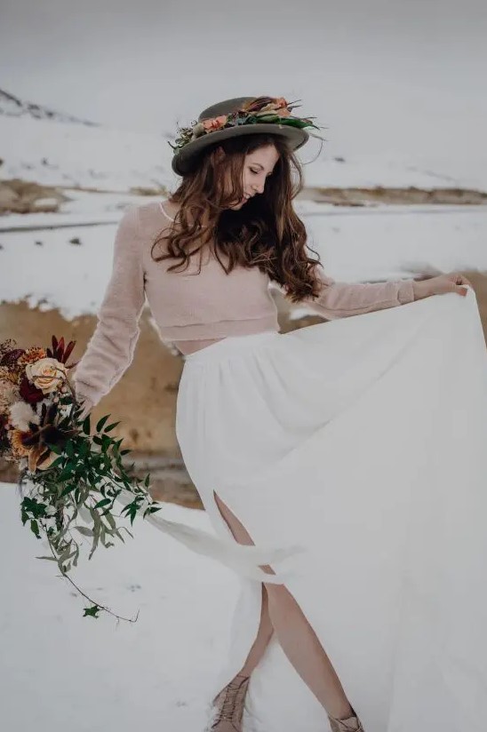 a blush crop top sweater with long sleeves, a white pleated skirt, tan booties and a grey hat decorated with fresh blooms