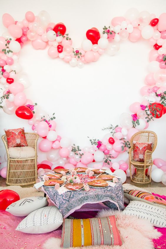 a bridal shower picnic setting with a low table, pillows, a balloon and flower heart as a party backdrop