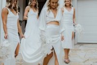 a bride wearing a neutral twisted crop top with puff sleeves and a maxi skirt with a slit, gold mules and a veil