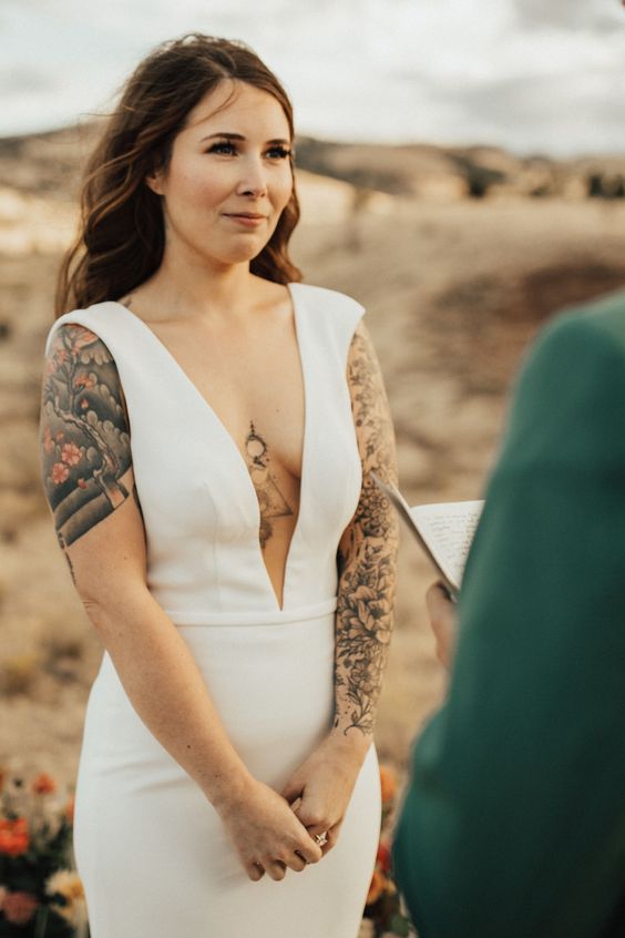 a bride wearing a plain fitting wedding dress with thick straps to show off her tattoos on the arm, body and shoulder