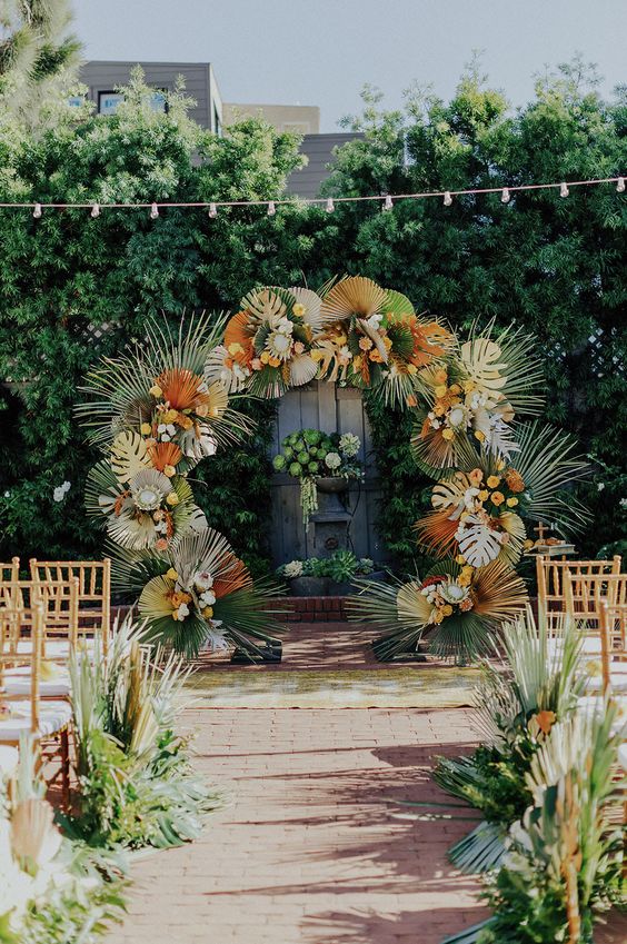 a bright round tropical wedding arch with tropical leaves, dried and spray painted ones, and fronds