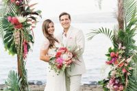 a bright tropical wedding arch topped with monstera leaves, pink, blush and purple blooms and cascading elements