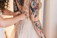 a chic A-line wedding dress with a blush gold embellished bodice and blush skirt, and no sleeves and a cutoutback show off the bold bride’s tattoos