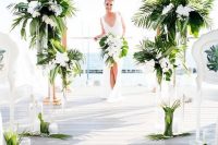 a chic wedding arch fully covered with tropical leaves and white orchids and matching arrangements to line up the aisle