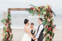 a colorful wedding arch decorated with lush tropical leaves and bold tropical blooms in green, pink and red