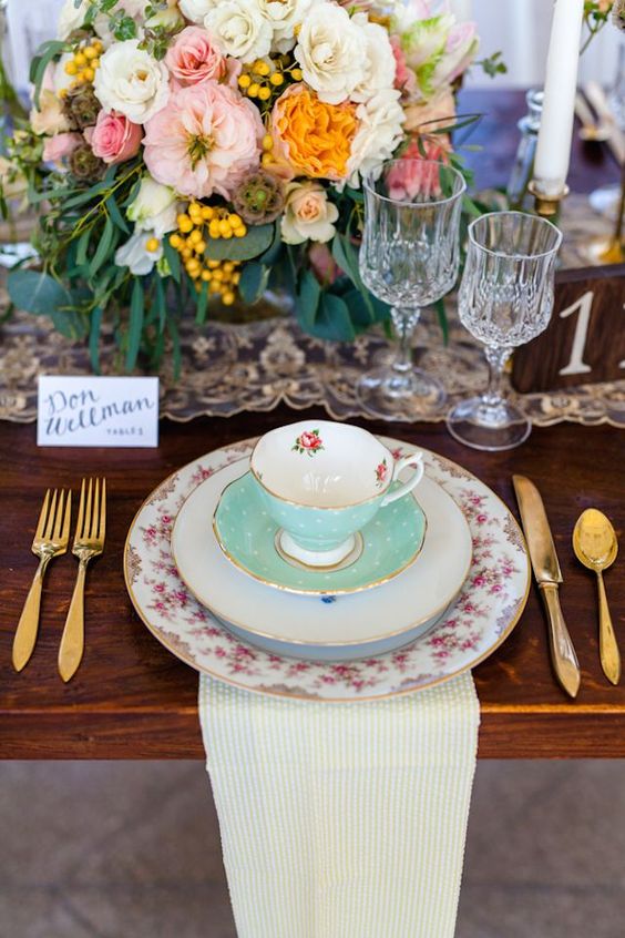 a cute vintage tea party setting with vintage porcelain, gold cutlery and lush blooms