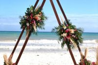 a double triangle wedding arch decorated with pampas grass, yellow and fuchsia blooms and tropical leaves
