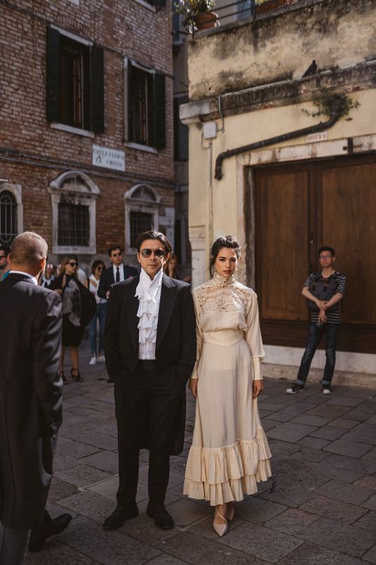 a groom wearing a white vintage shirt, black pants and a dinner jacket, a bride rocking a unique neutral midi dress with ruffles and lace applique