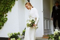 a lace wedding dress paired with a cover up and white shoes plus statement earrings for an ultra-modern bridal look