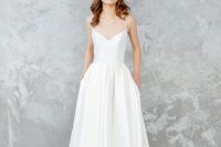 a lovely minimalist A-line wedding dress with a V-neckline, spaghetti straps, a pleated skirt with pockets and minimalist strap heels