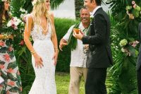 a lush greenery wedding arch dotted wih pink blooms is a nice idea for a tropical wedding