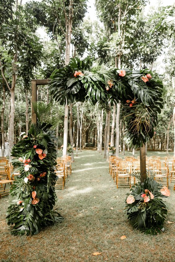 a lush tropical wedding arch decorated with monstera leaves and pink flowers is elegant