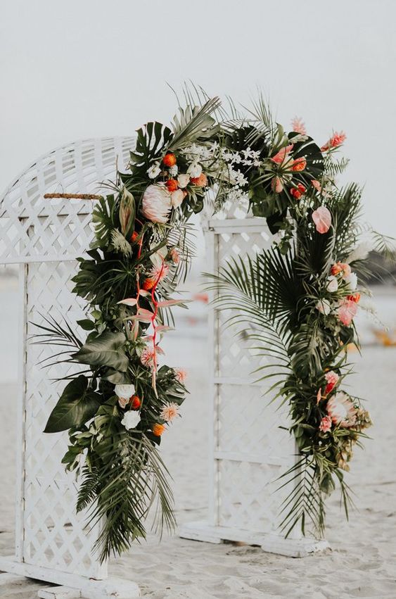 a luxurious tropical wedding arch decorated with leaves, white, orange and pink blooms is very chic