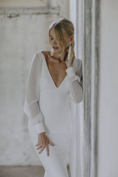 a modern and elegant wedding dress with a fitting silhouette, a plunging neckline, long sleeves and tassel earrings