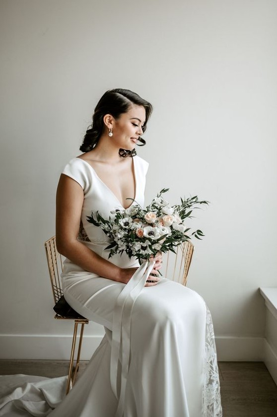 a modern glam bridal look with a plain fitting silk wedding dress with lace inserts, a deep neckline and cap sleeves plus statement pearl earrings