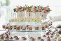 a modern oversized glass tiered dessert stand with bright pink blooms and greenery in vases is a cool idea for any modern wedding