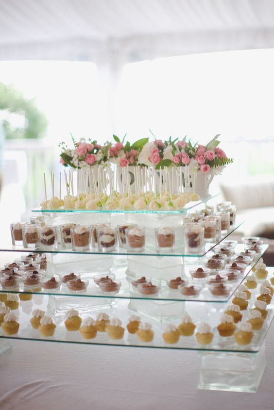 a modern oversized glass tiered dessert stand with bright pink blooms and greenery in vases is a cool idea for any modern wedding