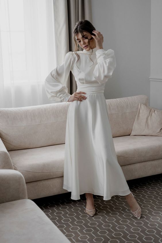 a modest and chic white silk midi wedding dress with puff sleeves, a high neckline, sheer embellished shoes