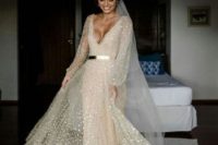 a neutral sparkling A-line wedding dress with a plunging neckline, long sleeves and a veil