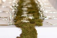 a neutral wedding reception table with a white tablecloth and a moss table runner over it, candles and small blooms is a lovely idea for an Iceland wedding