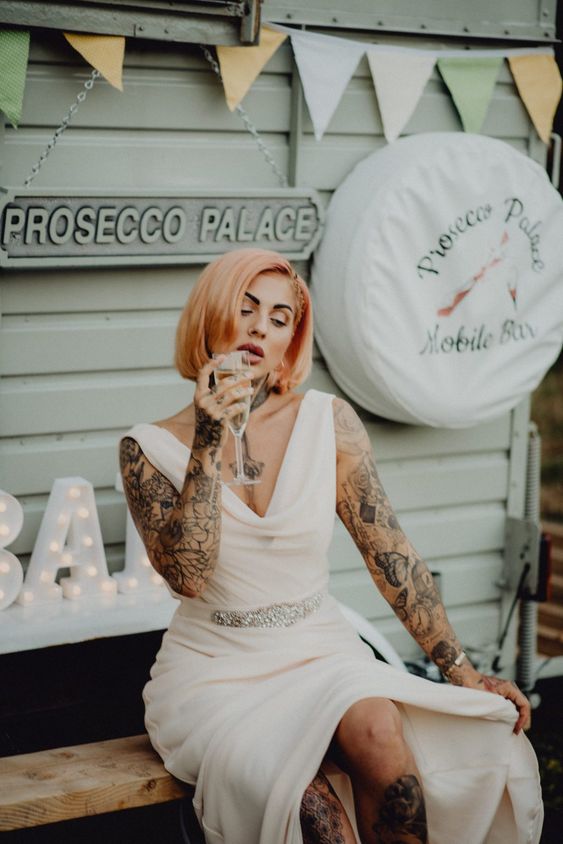 a plain draped A-line wedding dress showing off tattoos on the legs, arms and chest plus neck