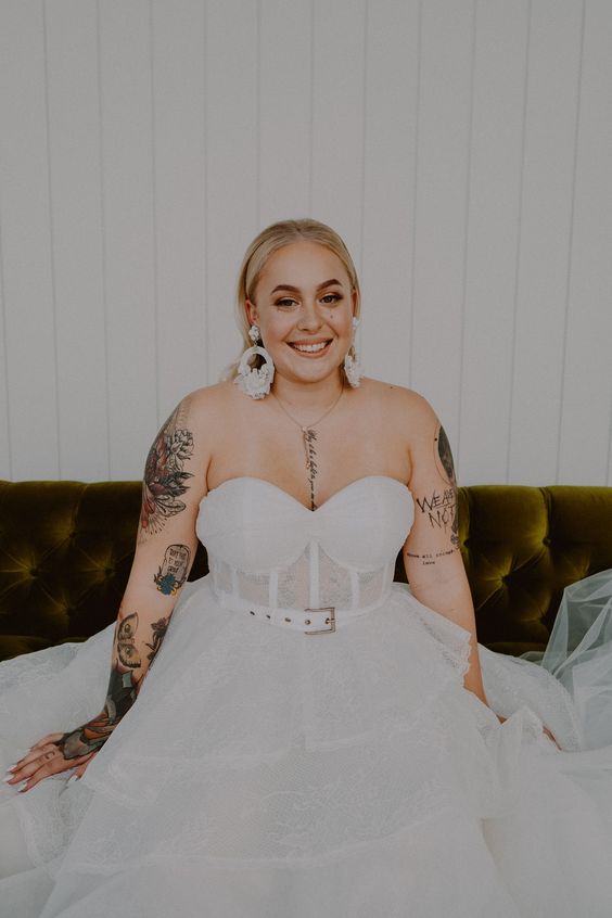 a pretty strapless wedding ballgown with a belt showing off bride's tattoos on the shoulders and arms plus on the chest