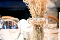 a rustic centerpiece with a mirror, a jar with wheat and twine and lace