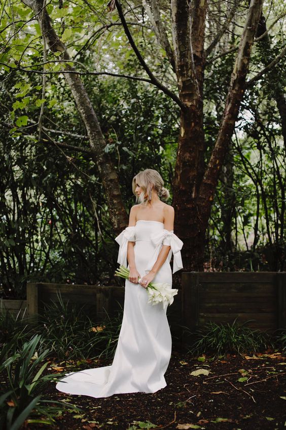 a silk off the shoulder wedding dress with bows on the arms, a train is a lovely idea for a minimalist bride