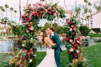 a spectacular wedding arch decorated with greenery and monstera leaves, pink, red and blush blooms and fronds