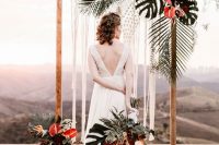 a statement wedding arch decorated with macrame, tropical leaves and red flowers is very bold