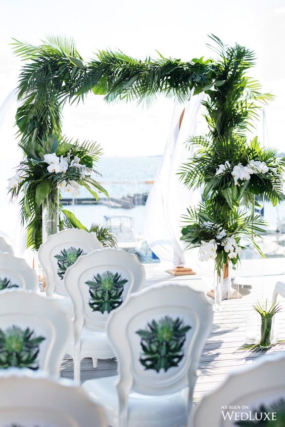 a stylish tropical wedding arch decorated with lush tropical leaves and white orchids is very elegant