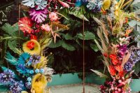 a super colorful tropical wedding arch done with spray painted fronds and leaves, grasses and blooms in all the colors of rainbow