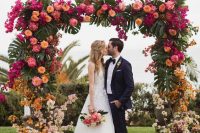 a super lush tropical wedding arch covered with monstera leaves, orange, pink, blush and rust blooms