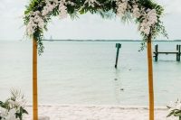 a tropical wedding arch covered with greenery and tropical leaves and white lilies and orchids is very refined