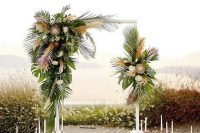 a tropical wedding arch with leaves, king proteas and pampas grass is stylish and boho-inspired
