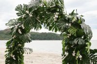 a very lush tropical wedding arch decorated with monstera leaves and white orchids is very sophisticated
