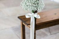 a wooden bench in the wedding aisle accented with a white silk bow with a baby’s breath arrangement looks amazingly chic