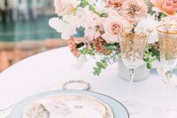 an exquisite wedding reception table with blush and mauve blooms and greeneyr, a blue charger and printed plates with gold rims and a paper fan as a menu