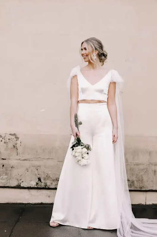 an ultra-modern bridal look with a plain silk crop top with a deep V-neckline and a tulle capelet, high waisted wideleg silk pants and nude shoes