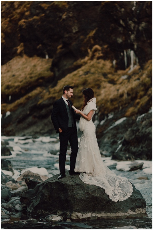 elegant wedding outfits with a black suit, a grey waistcoat and burgundy tie for the groom, a refined lace mermaid wedding dress with a train for the bride