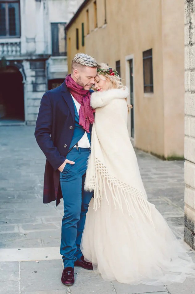 the groom wearing a bold blue suit, a navy coat, burgundy moccasins and a burgundy scarf