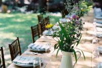 a backyard rehearsal dinner tablescape with neutral placemats, plaid napkins, bright wildflowers in a jug and simple silver