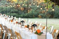 a bbq rehearsal dinner tablescape with candle lanterns, foliage and pumpkins, lights over the table