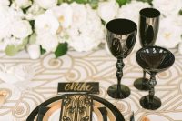 a beautiful neutral tablescape inspired by 1920s, with lots of white blooms, a white and gold tablecloth, a black charger and a napkin plus some glasses