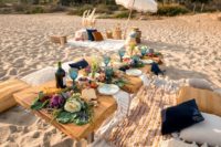 a boho beach picnic with boho rugs, pillows, candles, blue glasses, a vegetable table runner and a lounge zone with an umbrella